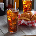 A Libbey stackable plastic beverage glass filled with ice tea and lemon slices on a table with onion rings.