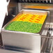 A stainless steel pan filled with peas and carrots in a Crown Verity steam pan adapter on a counter.