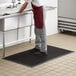 A man in an apron standing on a black anti-fatigue floor mat at a sink.
