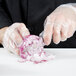 A person in a plastic glove using a Dexter-Russell DuoGlide paring knife to peel and slice a red onion.