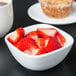 A CAC Citysquare white porcelain bowl filled with strawberries on a white surface.