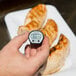 A hand holding a Taylor digital pocket probe thermometer over a plate of chicken.