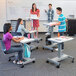 A group of students sitting at a Luxor adjustable height standing desk in a classroom.