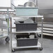 A Vollrath stainless steel utility cart with three shelves holding white bowls.