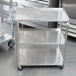 A Vollrath stainless steel utility cart with three shelves in a kitchen.