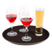 A Thunder Group non-skid serving tray holding three drinks with a glass of beer, a glass of orange liquid, and a glass of red liquid.