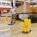 A woman using a Rubbermaid yellow mop bucket to mop the floor.