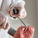 A person in white gloves using a Backyard Pro T-shaped boning hook to cut meat on a counter.