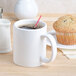 A white Tuxton china mug filled with coffee on a table with a muffin.