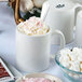 A close-up of a Tuxton white china mug with whipped cream and marshmallows.