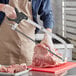 A man using a Backyard Pro stainless steel butcher hand meat saw to cut meat on a cutting board.