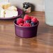 A Fiesta Mulberry china ramekin filled with raspberries on a table with bread.