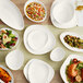 A table with Acopa Nova cream white triangle plates and bowls of food on it.