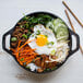 A Lodge mini cast iron wok filled with rice, vegetables, and a fried egg.