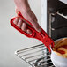 A close-up of a hand using an American Metalcraft red nylon pizza pan gripper to hold a deep dish pizza.