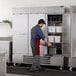 A man in a red apron opening the solid door of a Beverage-Air Horizon Series reach-in freezer.