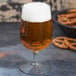 A Libbey Banquet goblet filled with beer with a bowl of pretzels on the table.