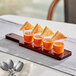 An Acopa mahogany flight paddle with three tasting glasses filled with orange liquid.