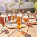 A group of people sitting at a wooden table with Arcoroc Linz Footed Pilsner glasses filled with beer.