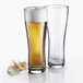 Two Arcoroc Oslo Pilsner glasses filled with beer on a white surface.