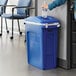 A woman putting a plastic bottle in a blue Rubbermaid trash can.
