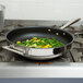 A Vollrath stainless steel non-stick fry pan with green beans and yellow peppers cooking on a stove.