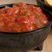 A black melamine molcajete bowl filled with salsa and chips on a wooden table.