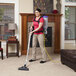 A woman wearing a red shirt using a ProTeam Super CoachVac backpack vacuum to clean a carpet.