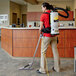 A woman using a ProTeam backpack vacuum cleaner to vacuum a room.