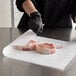A person in black gloves cutting meat on a Choice white butcher paper sheet.