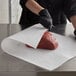 A person cutting raw meat on a table with Choice white butcher paper.