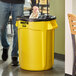 A man holding a yellow Rubbermaid BRUTE trash can.