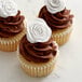 Three cupcakes with Satin Ice ChocoPan white modeling chocolate roses on top.