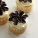 A group of cupcakes with chocolate frosting and Satin Ice ChocoPan chocolate flowers.