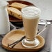 A glass of UPOURIA Sweet French Vanilla Cappuccino with foam on top next to a spoon.