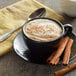 A cup of UPOURIA Pumpkin Spice Cappuccino with cinnamon sticks and a spoon.