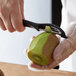 A person using a Victorinox black straight serrated vegetable peeler to peel a kiwi.