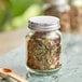 An Acopa Rustic Charm mini mason jar filled with dried herbs with a wooden spoon in it.