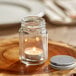 An Acopa Rustic Charm mini mason jar with a candle inside on a wooden table.