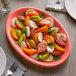 A Tuxton Cinnebar oval china coupe platter with tomatoes and mozzarella on a table.