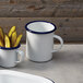 An American Metalcraft white enamel mug with a blue rim filled with pickles.