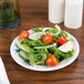 A Thunder Group Blue Bamboo melamine plate with salad, tomatoes, and cucumbers on a table.