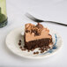 A piece of chocolate cake with chocolate chips and frosting on a Thunder Group Blue Bamboo melamine plate with a fork.