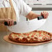 A close-up of a person using a Mercer Culinary Millennia Rocker Pizza Knife to cut a pizza.