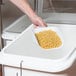 A hand holding a bowl of macaroni and cheese above a white Cambro ingredient bin.