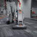 A man using a Hoover HushTone 15+ commercial bagged upright vacuum cleaner to clean a carpet in a corporate office.