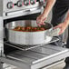 A person cooking food in a Choice aluminum brazier on a table in a professional kitchen.