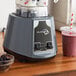 An AvaMix commercial blender with a bowl of blackberries and other fruit on a counter.