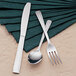 A Libbey stainless steel iced tea spoon, fork, and knife on a napkin on a table.
