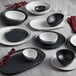 A dark gray irregular round matte melamine plate on a white surface with a table set with black and white dishes and bowls.